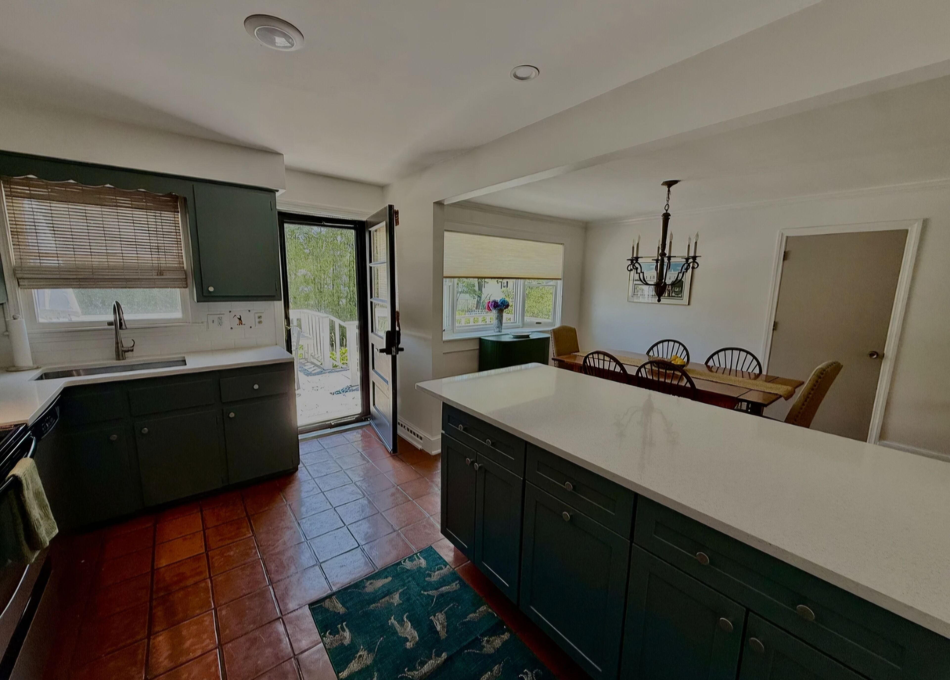 A modern kitchen with a large island, dark cabinetry, and a dining area with a chandelier.