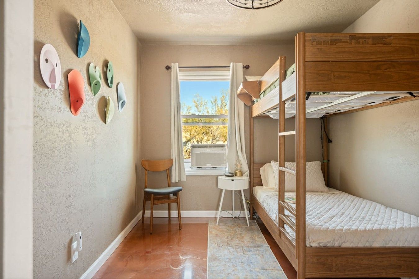 A compact room with a bunk bed, a chair, a small table, and a window with a view of trees.