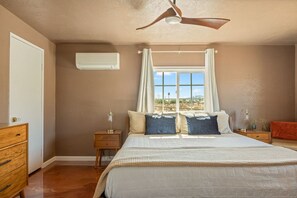 Ein Schlafzimmer mit einem Bett, Nachttischen, einem Deckenventilator und einem Fenster mit Vorhängen.