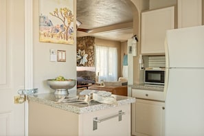A compact kitchen with a microwave, a bowl of fruit, and a dining area with a sofa and a decorative wall piece. - Aster Abode W/ Hot Tub & Game Room - 5 Mi to Park (Joshua Tree)
