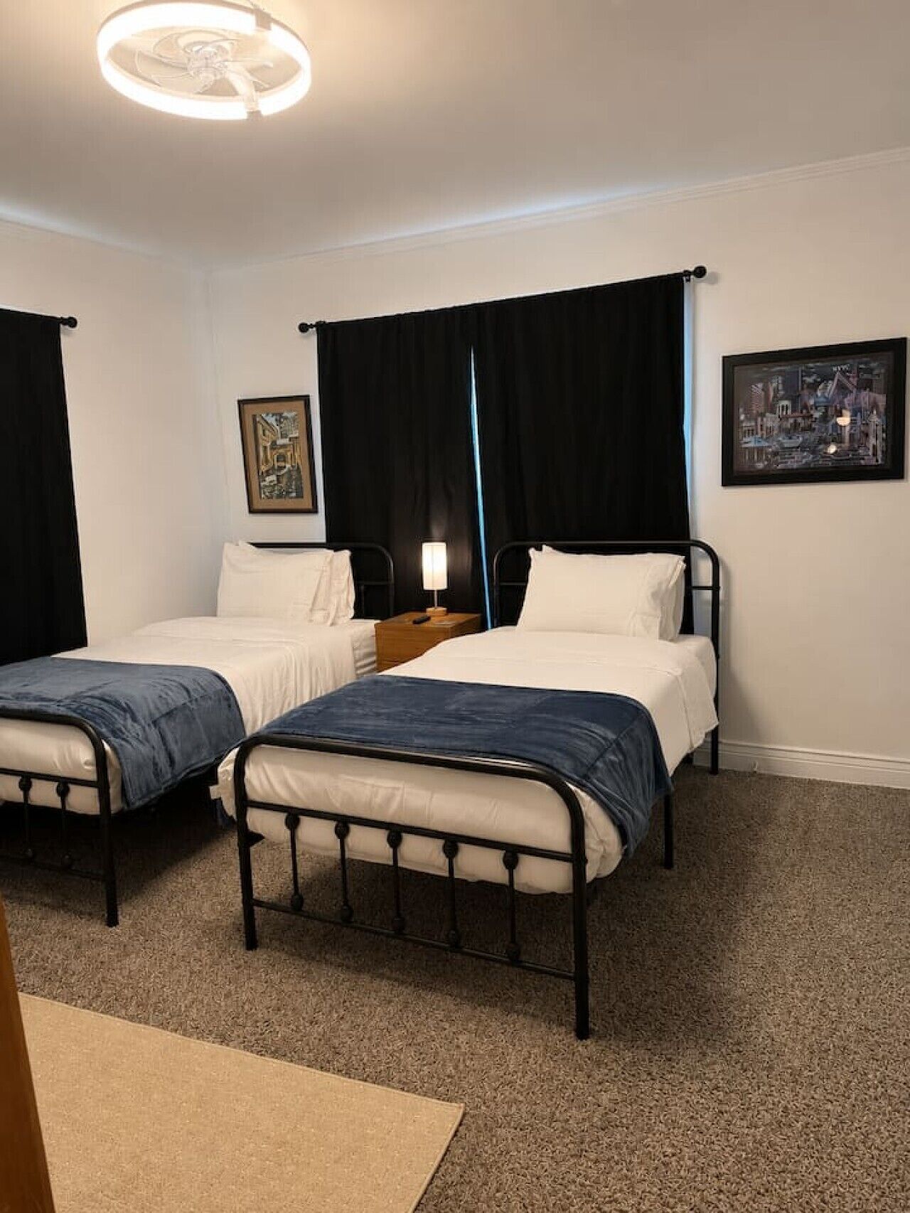 A hotel room with two single beds, a nightstand with a lamp, and a framed picture on the wall.