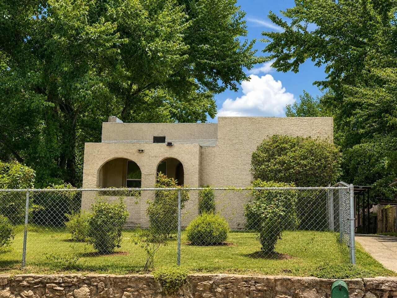 A building with a stone facade, arched windows, and a fenced yard with trimmed bushes.