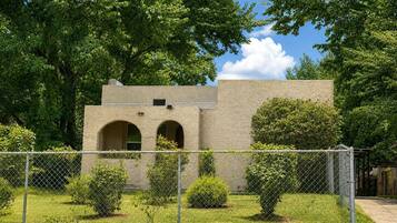 A building with a stone facade, arched windows, and a fenced yard with trimmed bushes.