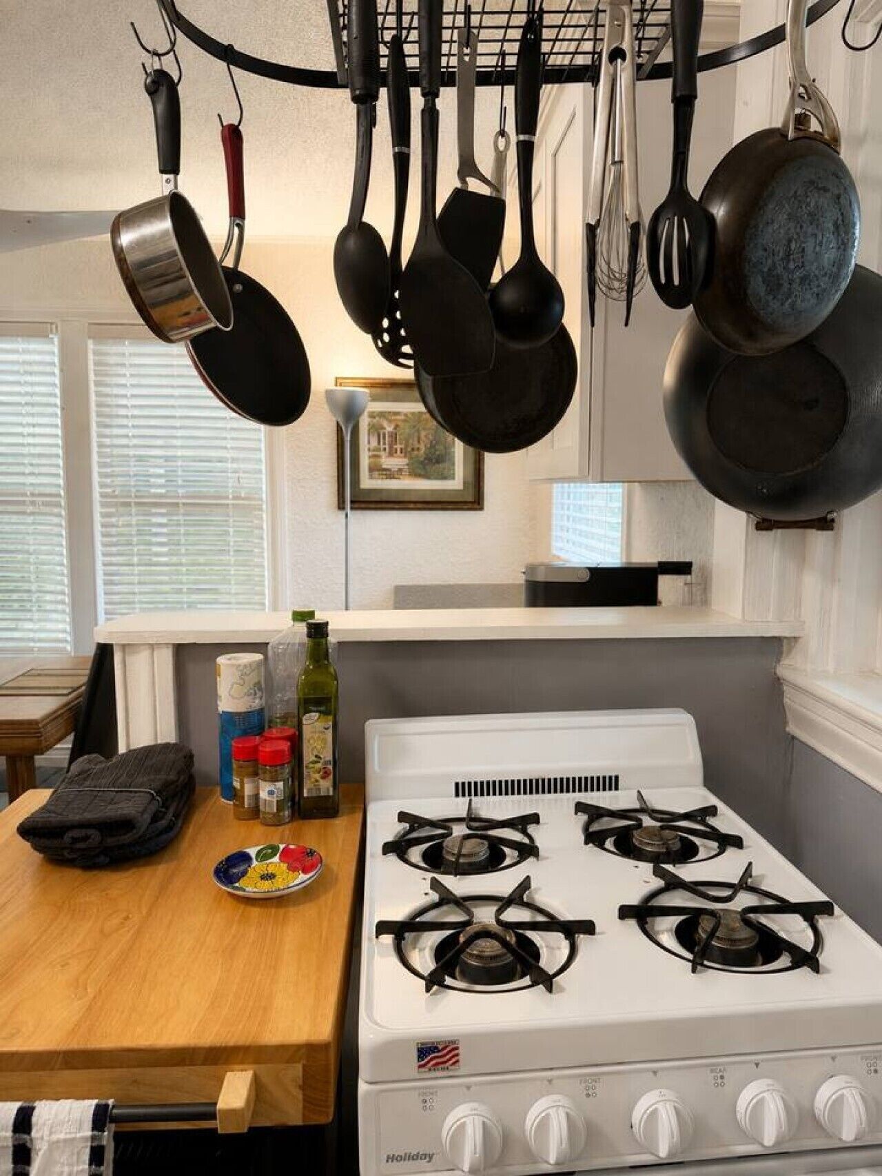 A kitchen with a white stove, hanging pots, and a wooden table with a plate of fruit.