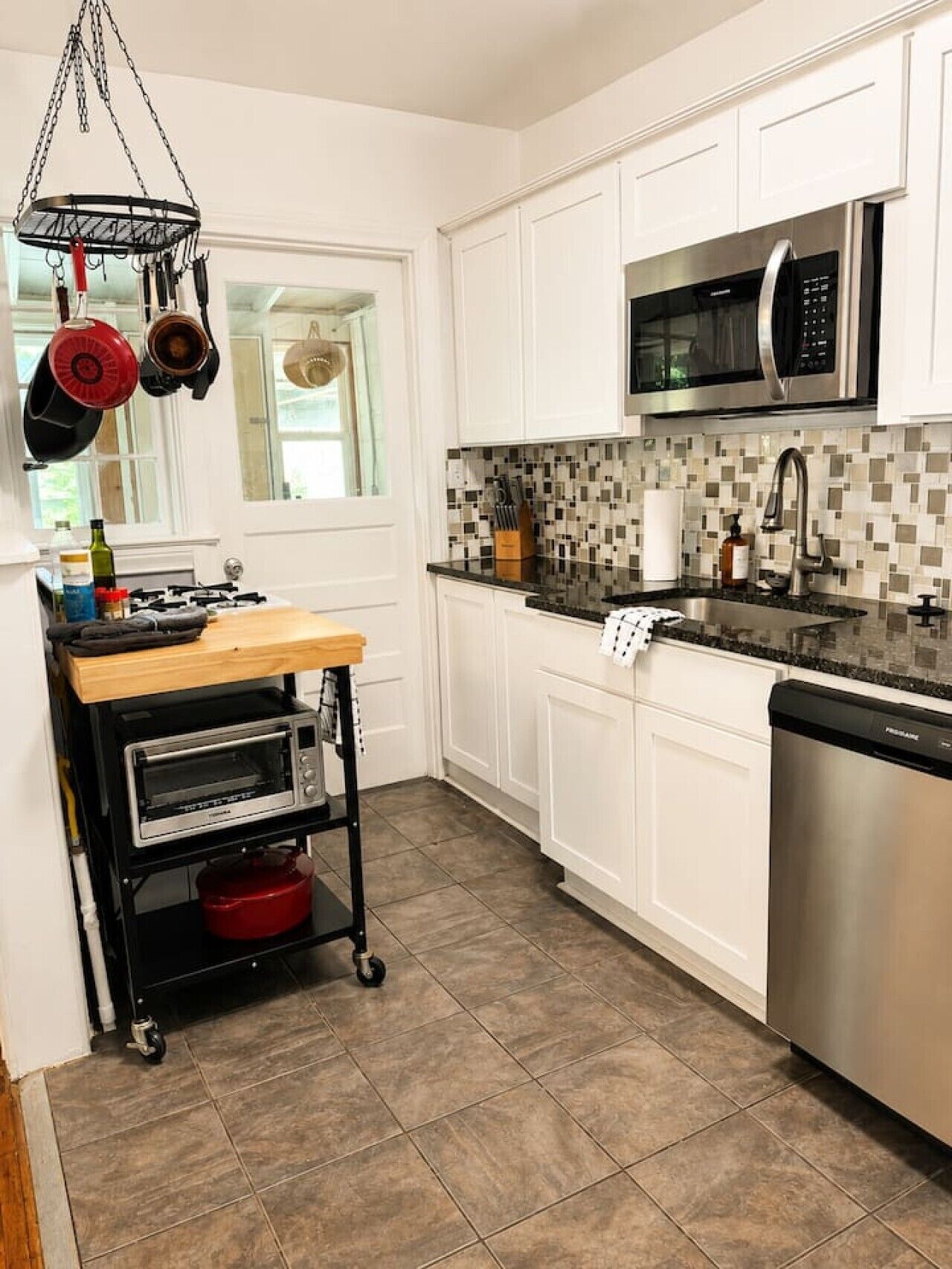 A kitchen with white cabinets, a microwave, a sink, and a portable oven cart.