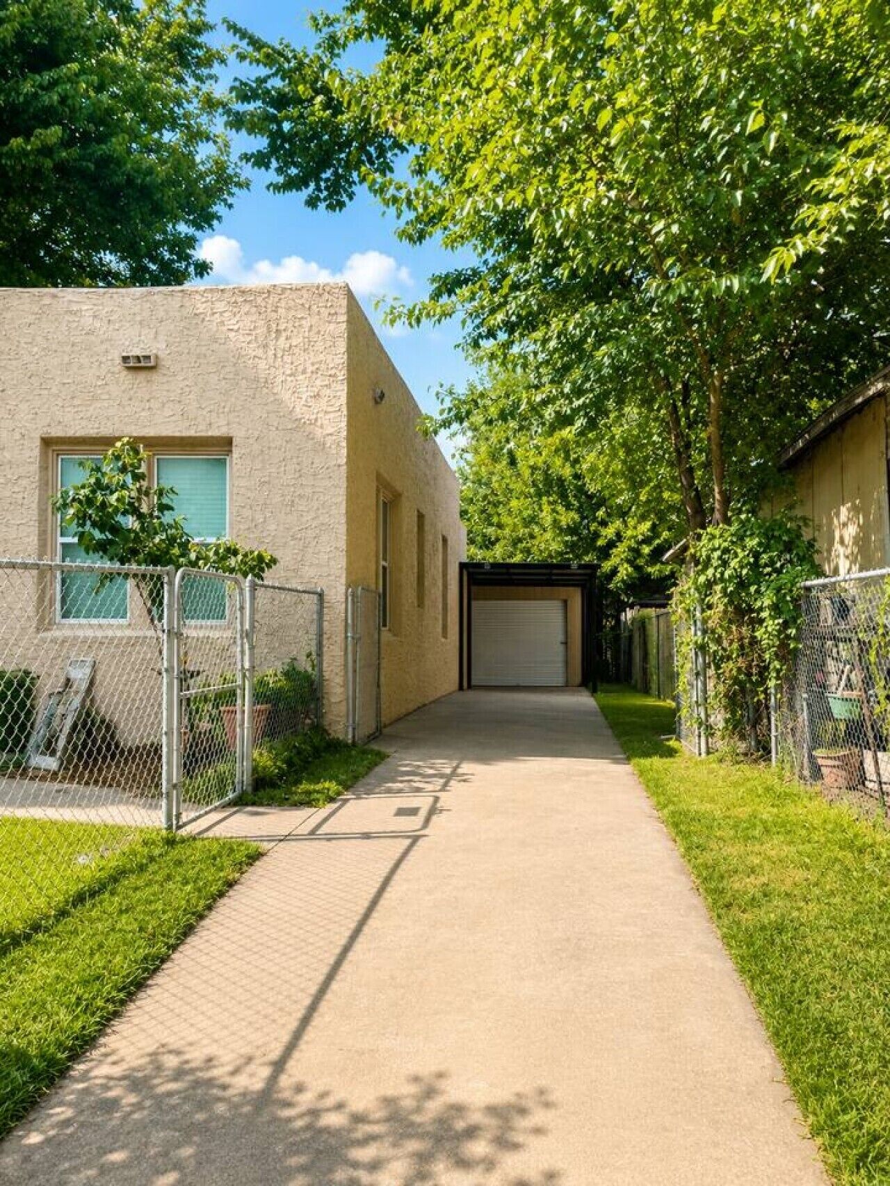 A pathway leading to a building with a garage door, surrounded by greenery and a chain-link fence.