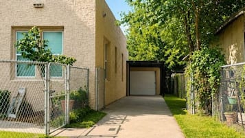 A pathway leading to a building with a garage door, surrounded by greenery and a chain-link fence.
