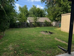 A backyard with a grassy lawn, a wooden shed, and a fenced area.