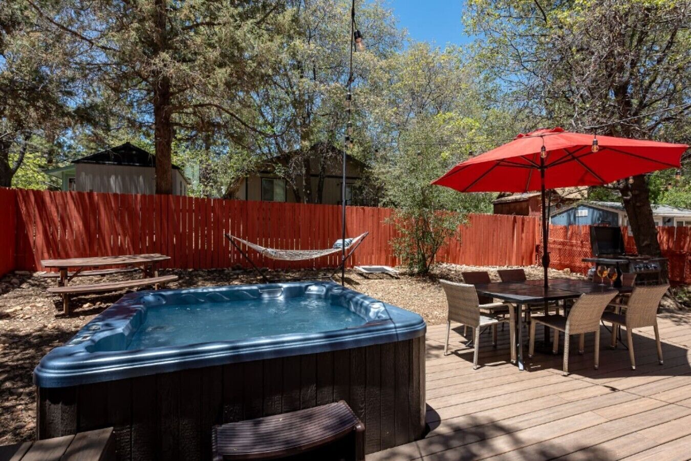 Un jardin avec un jacuzzi, une table de pique-nique, un hamac, un parasol rouge et un barbecue.