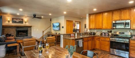 A spacious living area with a fireplace, a dining table set with glasses, and a kitchen with wooden cabinets and stainless steel appliances.