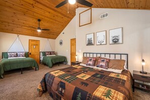 A bedroom with two single beds, a large bed with a patterned quilt, wooden ceiling, and wall-mounted artwork. - Pups and Pine Lodge | w/ BBQ Deck, Hot tub & Games (Big Bear)