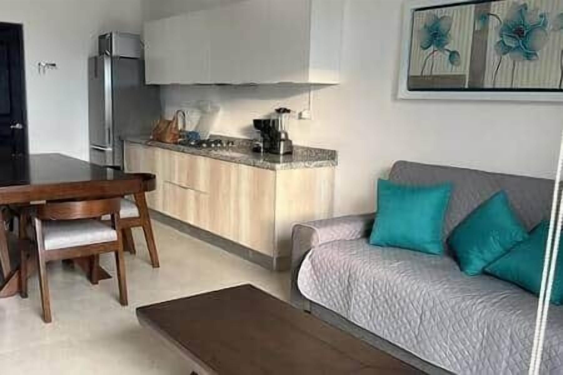 A compact living space with a kitchenette, a dining area, and a sofa with cushions.