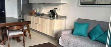 A compact living space with a kitchenette, a dining area, and a sofa with cushions.