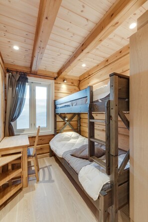 A wooden cabin interior with bunk beds, a table, and a window with curtains.