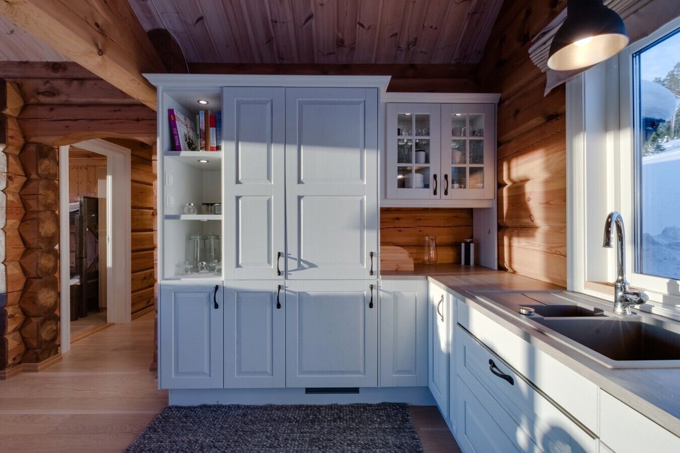 A modern kitchen with white cabinetry, a built-in oven, and a window with a view of a snowy landscape.