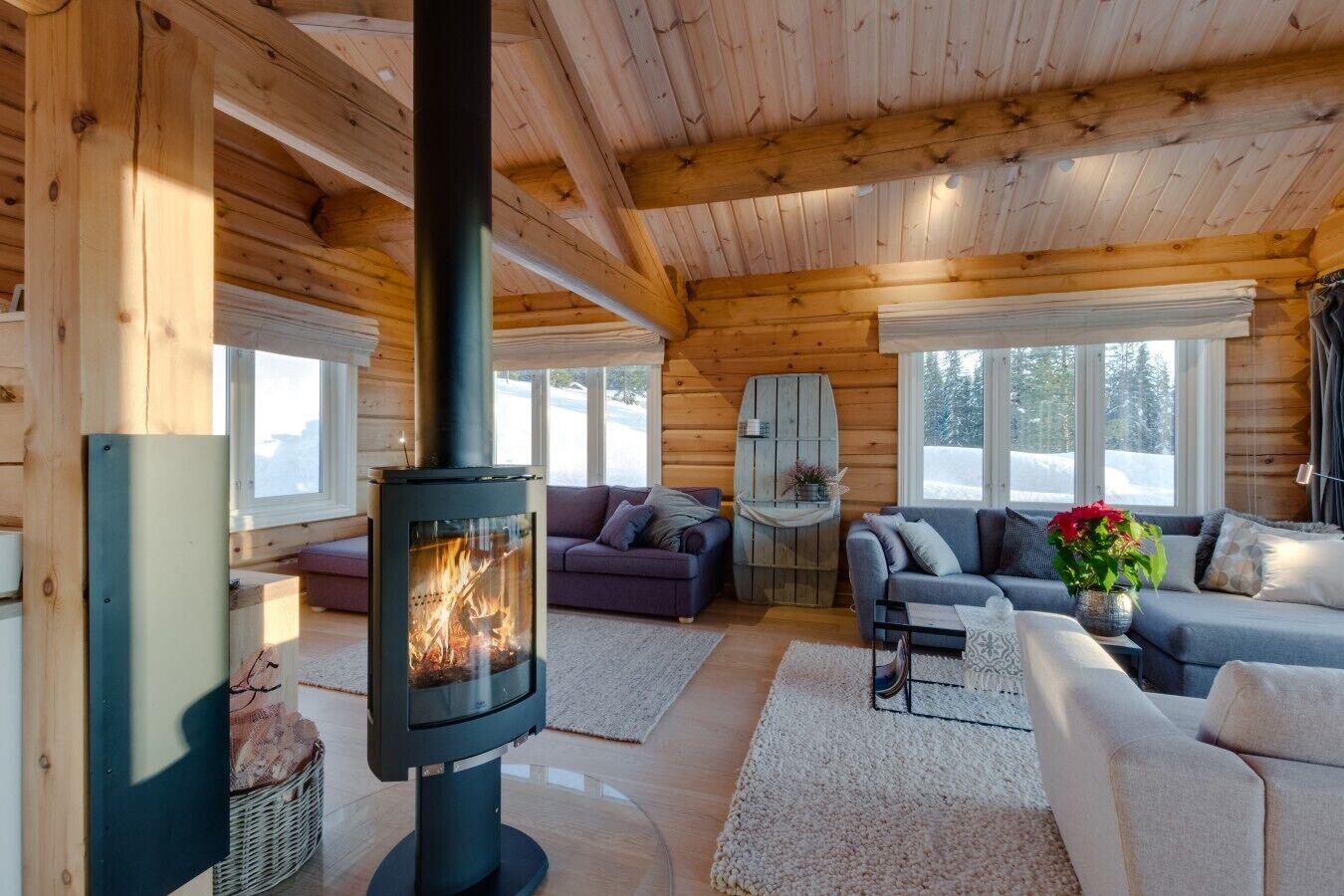 Interior acogedor de una cabaña con una estufa de leña, dos sofás y un ventanal grande.