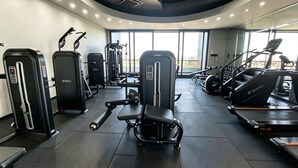 A gym with various exercise equipment, including treadmills and weight machines, and large windows allowing natural light.
