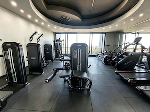 A gym with various exercise equipment, including treadmills and weight machines, and large windows allowing natural light.