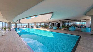 A modern indoor swimming pool with a view of the cityscape through large windows.