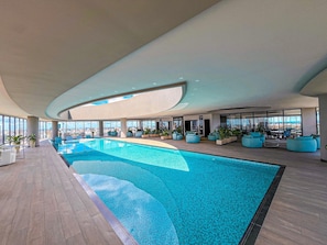 A modern indoor swimming pool with a view of the cityscape through large windows.