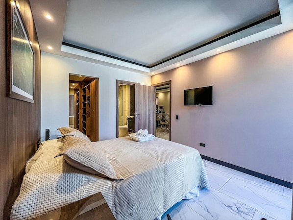 A hotel room with a bed, a TV, a bathroom, and a seating area.