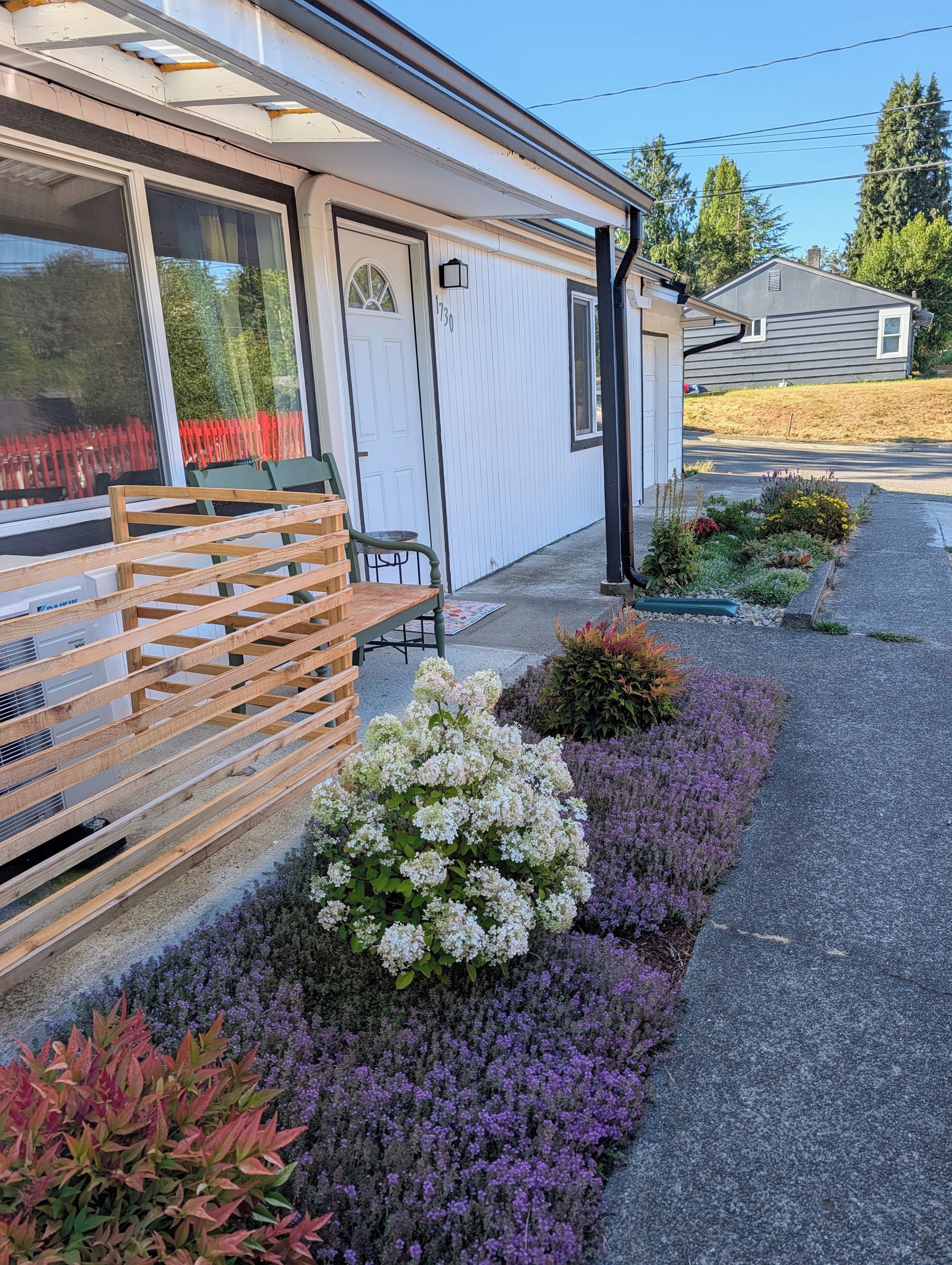 A residential property with a covered porch, a wooden bench, and a variety of flowering plants.