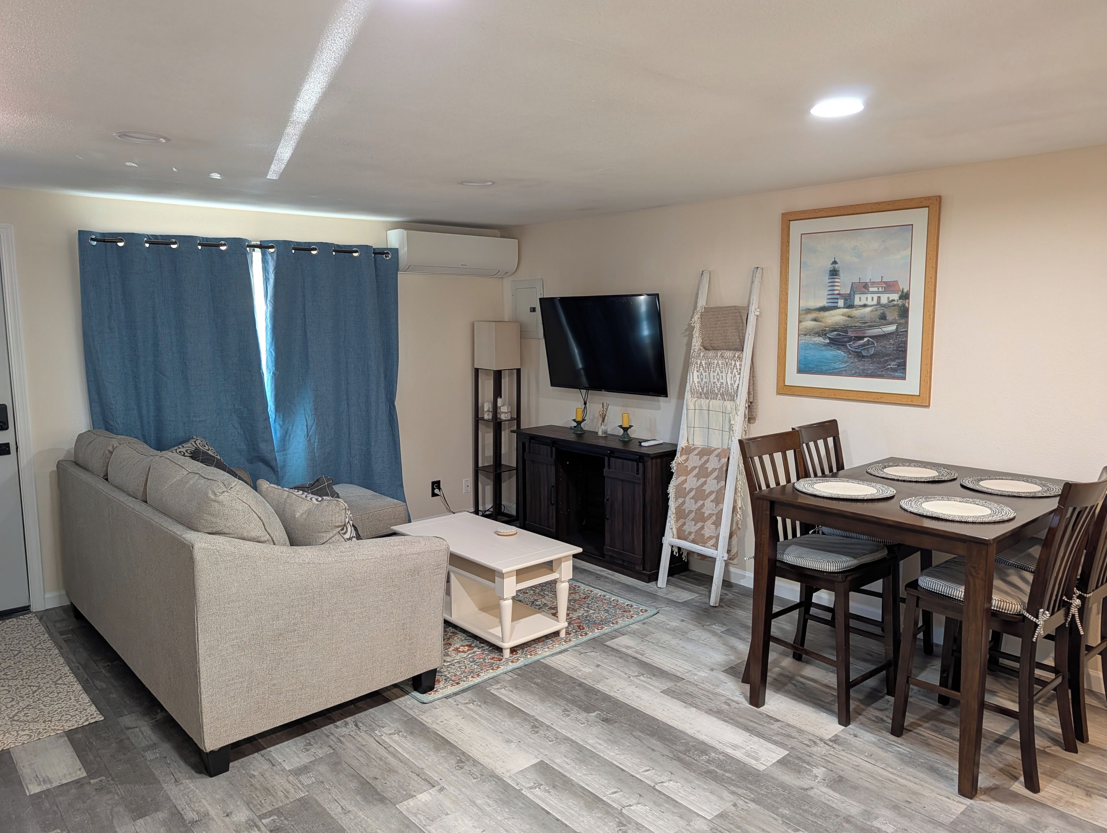 Uma sala de estar com sofá, televisão, mesa de jantar com cadeiras e um quadro na parede.