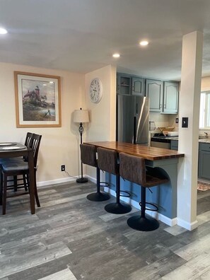Een moderne keuken met een bar, een eettafel met stoelen en een klok aan de muur.