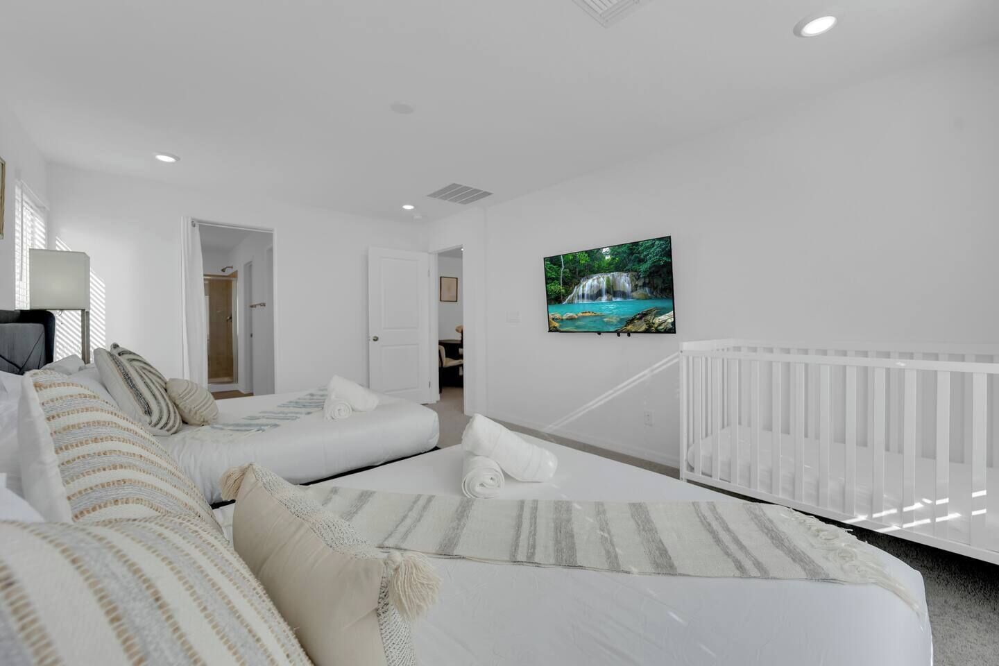 Une chambre à coucher avec un lit, un berceau blanc et un téléviseur fixé au mur.