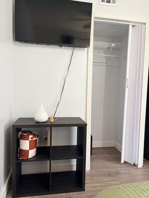 A room with a black TV mounted on the wall, a black console table with a white vase and a brown and white cushion, and a white closet with a door open. - Private 1-Bedroom Studio with Parking Near Orlando (Orlando)
