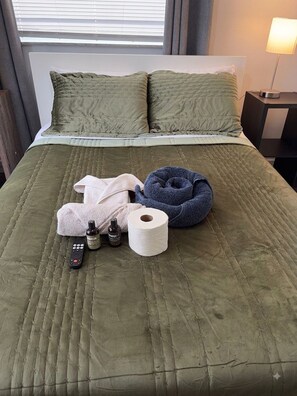 A bed with a green quilt, pillows, a remote control, toiletries, and a blue neck pillow. - Private 1-Bedroom Studio with Parking Near Orlando (Orlando)