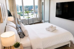 Ein Hotelzimmer mit Bett, Fernseher, Fenster mit Blick auf die Stadt und einem Sessel am Fenster.