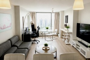 A modern living room with a sofa, coffee table, TV, and a dining area with a table and chairs. - Panoramic False Creek View 2BR/2BA | Pool, Parking (Vancouver)