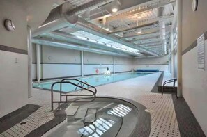 An indoor swimming pool with a diving board, a changing room, and a ceiling with visible ductwork. - Panoramic False Creek View 2BR/2BA | Pool, Parking (Vancouver)