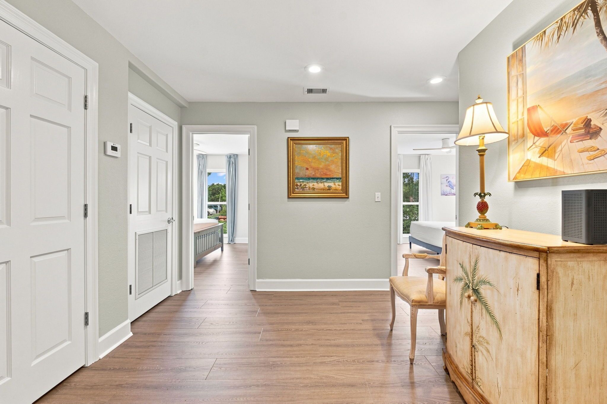 A hallway with a wooden floor, white doors, a painting on the wall, and a lamp on a cabinet.