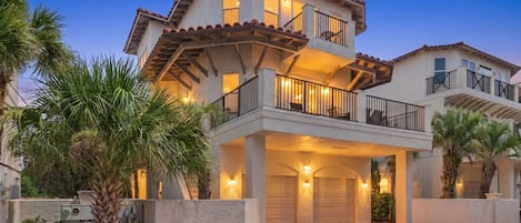 A multi-story residential building with a two-story balcony, a garage, and a well-lit entrance.
