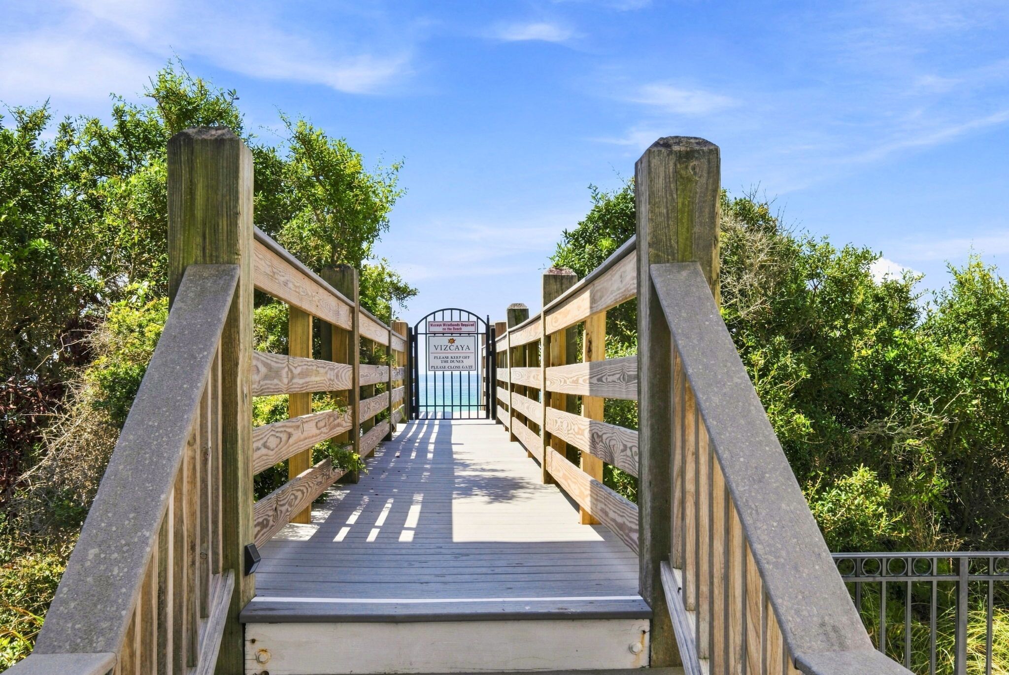 A wooden pedestrian bridge with a metal gate at the end, surrounded by greenery.
