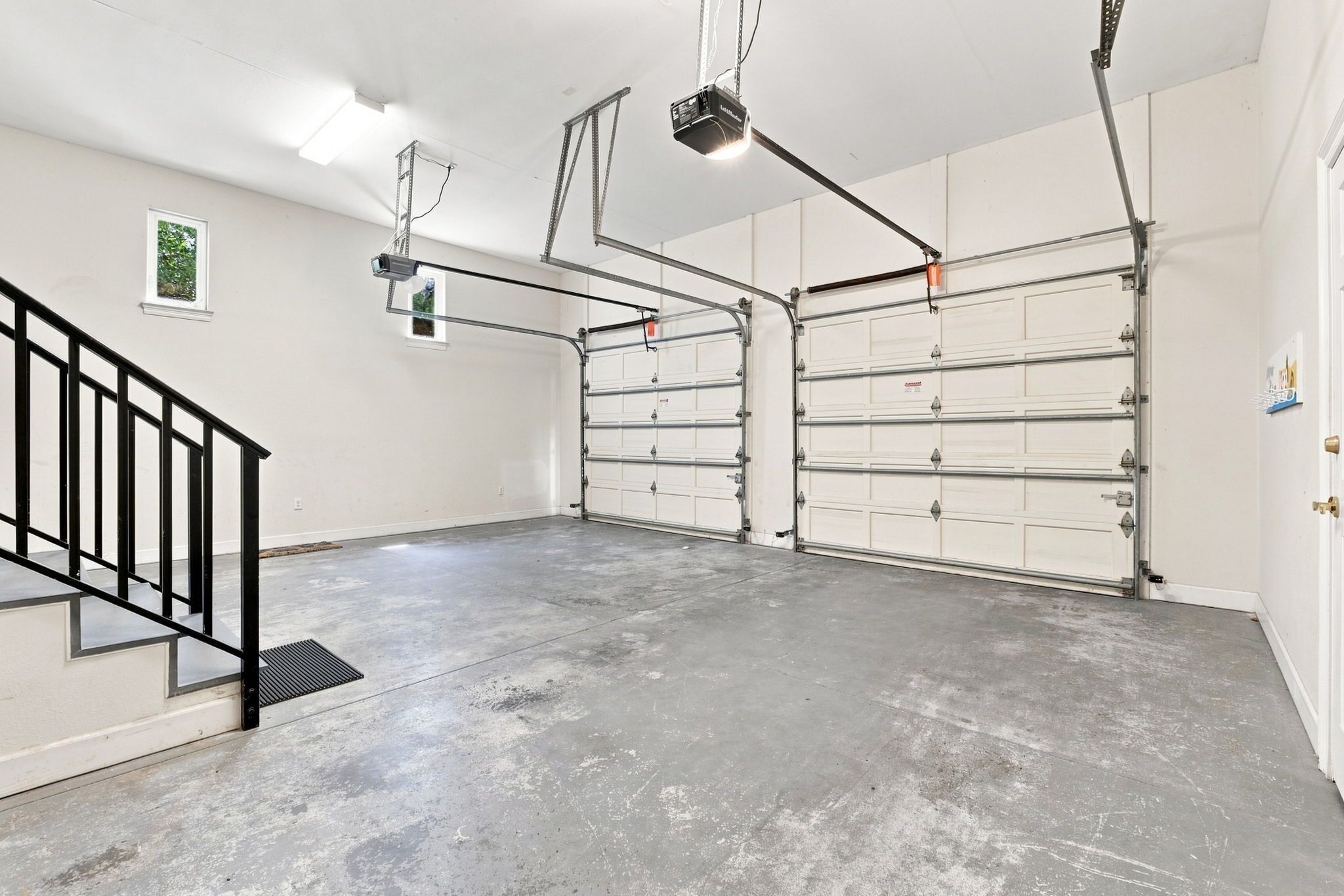 A garage with a concrete floor, a black metal staircase, and a ceiling-mounted projector.