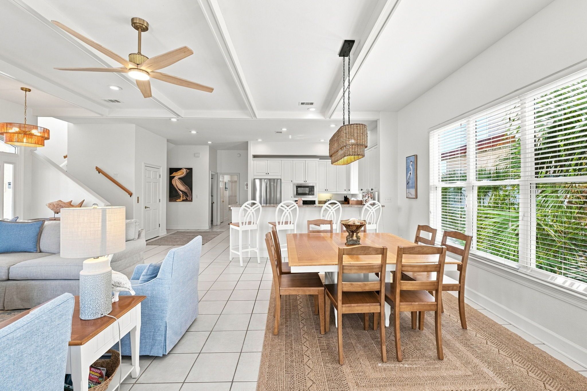A modern kitchen with white cabinets, a dining area with a wooden table and chairs, and a ceiling fan.