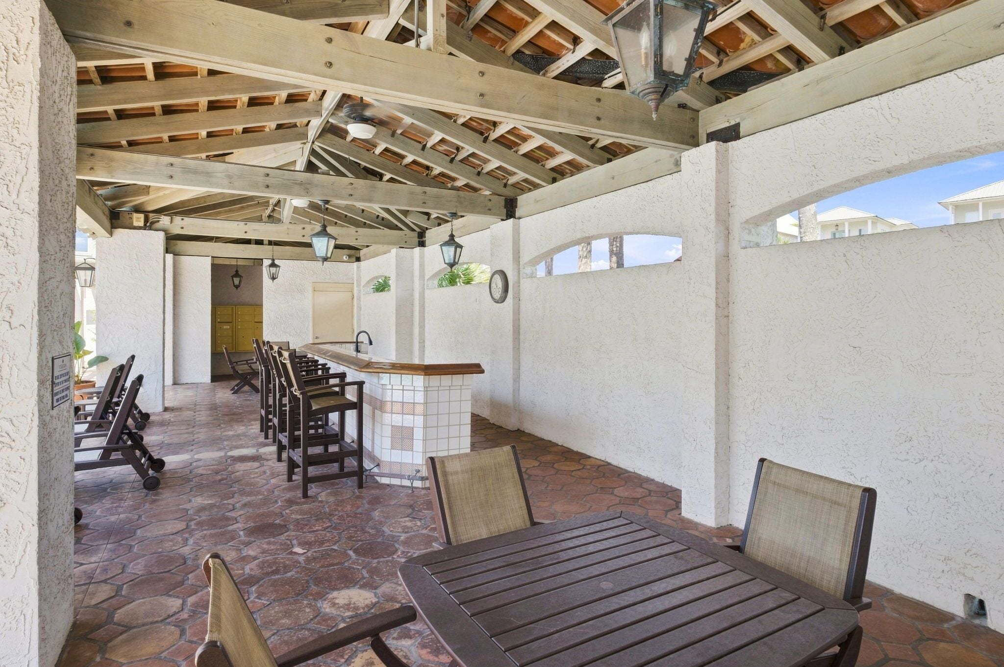 A covered patio area with a wooden table and chairs, a tiled bar counter, and a view of the surrounding buildings.