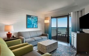 A hotel room with a sofa, a small table, a television, and a balcony with a view. - Spacious Family Beach Stay | Pools, Hot Tubs & Ocean Views | Close to SkyWheel (Myrtle Beach)