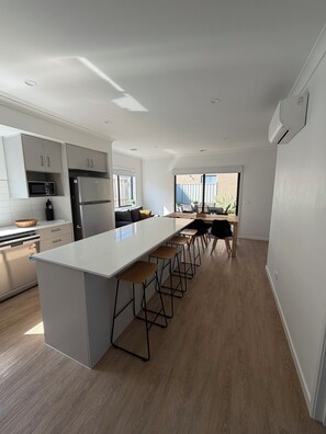 A modern kitchen with a central island, bar stools, and a view to the outside. - Modern cozy home opp park in quiet neighbourhood (Cranbourne East)