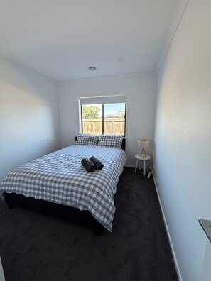 A bedroom with a bed, a window, a bedside table, and a view of the outside. - Modern cozy home opp park in quiet neighbourhood (Cranbourne East)