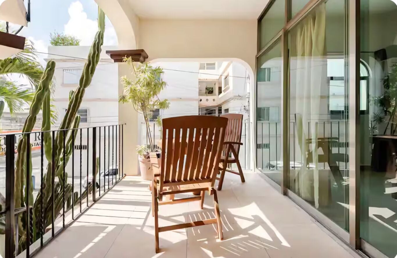 Ein Balkon mit einem Holzstuhl, Blumentöpfen und einer Glastür, die zu einem Innenraum führt.