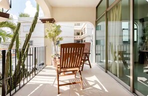 A balcony with a wooden chair, potted plants, and a glass door leading to an interior space. - La Luna: Apartment with rooftop lounge access steps from 5 Avenida (Playa del Carmen)