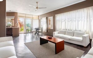 Ein geräumiges Wohnzimmer mit einem weißen Sofa, einem Couchtisch und einem Essbereich mit Stühlen.
