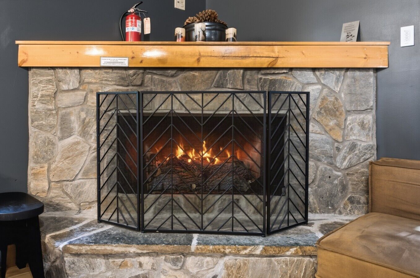 Une cheminée en pierre avec un feu de bois, une étagère en bois au-dessus du foyer et un extincteur.