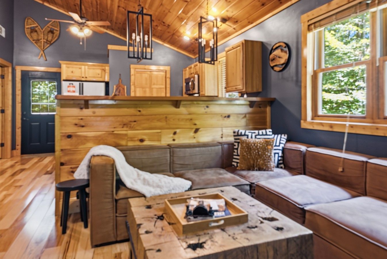 L’intérieur chaleureux d’un chalet avec un plafond en bois, un banc intégré servant de coin salon et une petite cuisine.