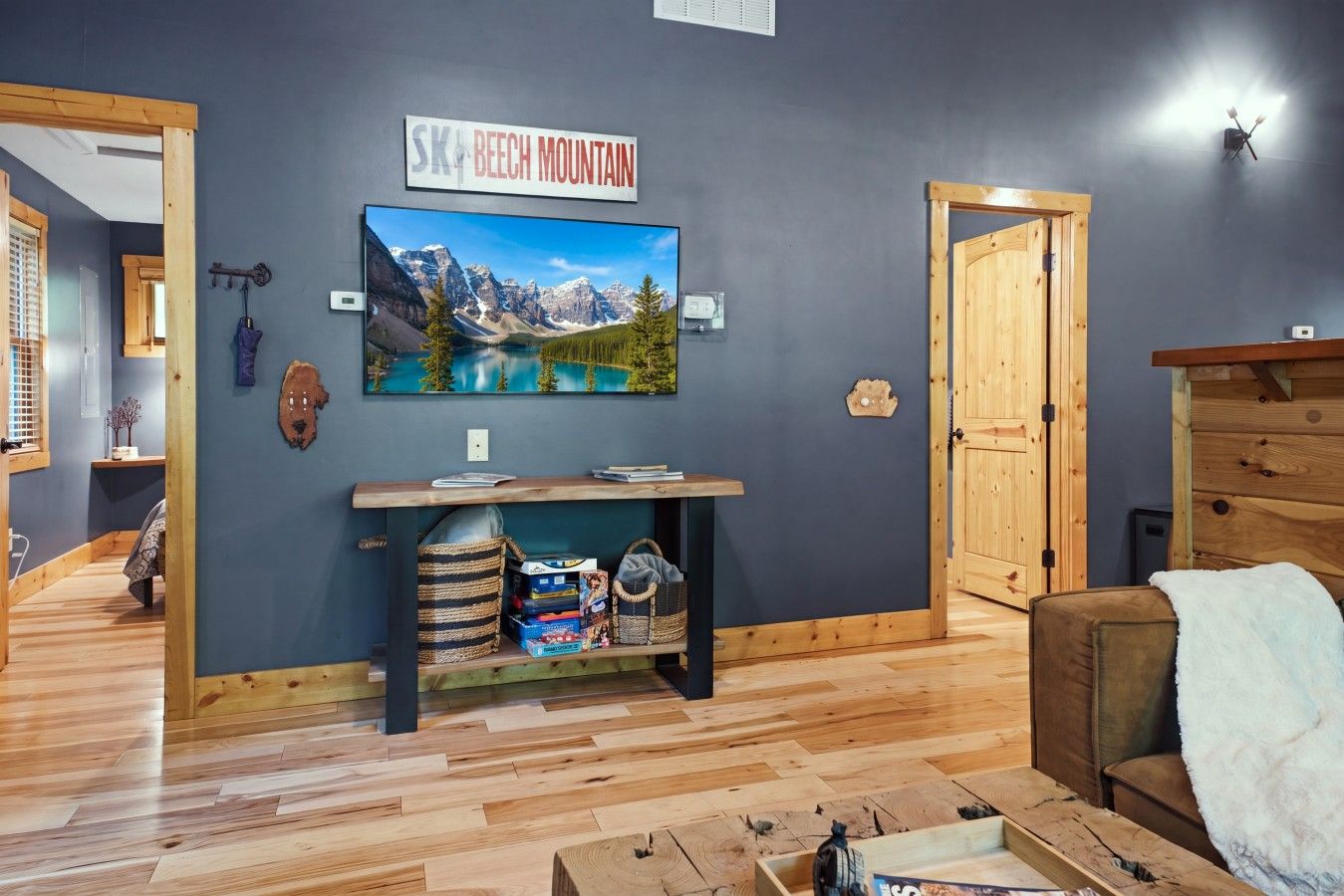Een kamer met een tv waarop een berglandschap te zien is, een houten plank met boeken en tassen, en een gezellige zithoek met een kussen.