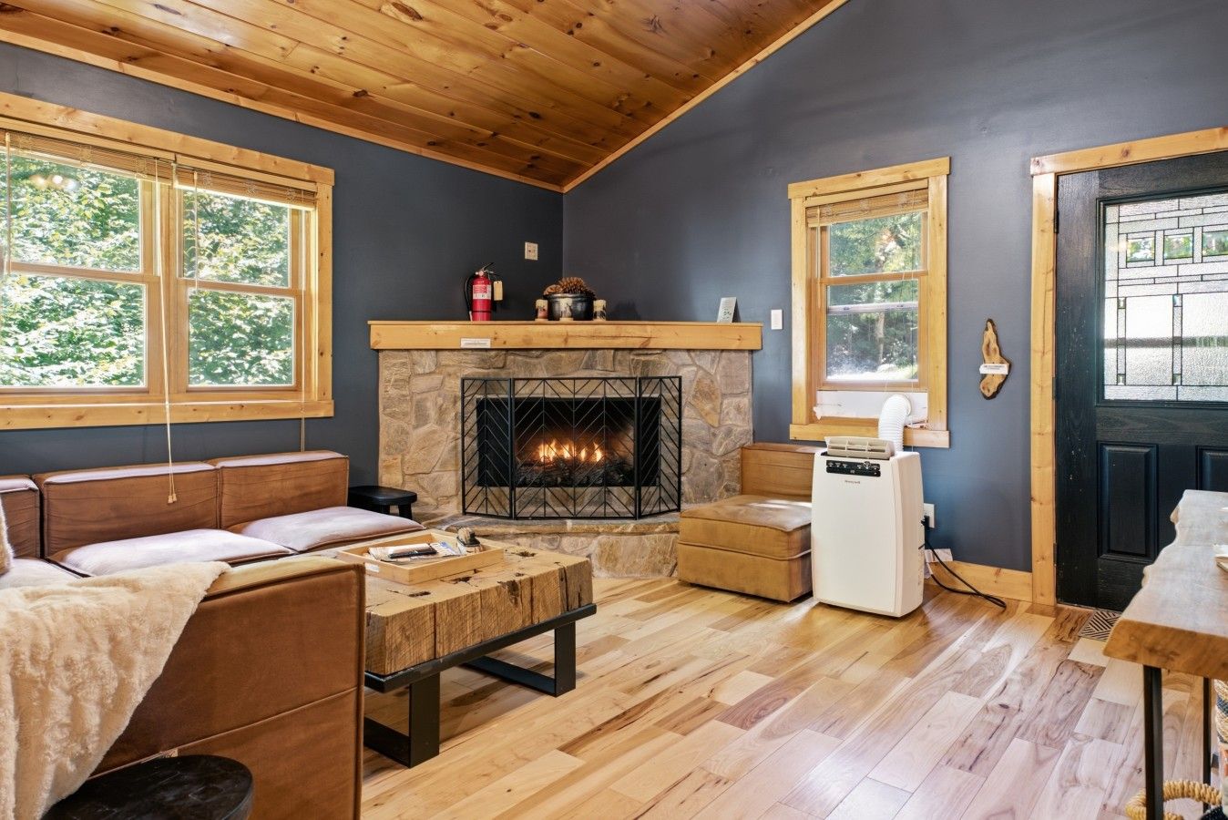 A cozy room with a fireplace, wooden furniture, and large windows.
